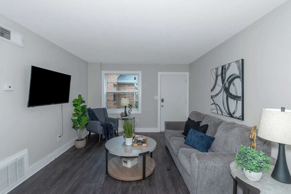 A modern living room with a flat-screen TV, grey sofa, round coffee table, and potted plants. - Central Buckhead 2BR apartment with king beds, full kitchen, fast Wi-Fi, and free parking — minutes from Lenox Square, Phipps Plaza, and top dining. (Atlanta)