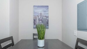 A dining area with a table, chairs, a potted plant, and a cityscape painting on the wall. - Central Buckhead 2BR apartment with king beds, full kitchen, fast Wi-Fi, and free parking — minutes from Lenox Square, Phipps Plaza, and top dining. (Atlanta)