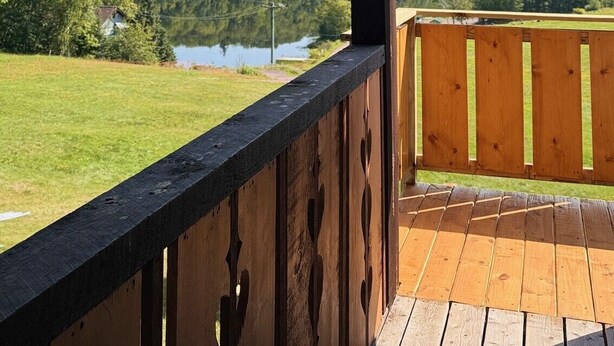 Een houten terras met uitzicht op een meer en beboste heuvels.