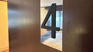 Een donkere muur met het getal '4' en een klein raam dat een interieur van een kamer weerspiegelt.
