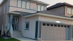 A two-story house with a garage, a front porch, and a staircase leading to the entrance. - Devonshire Cozy Haven (Winnipeg)