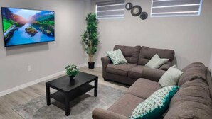 A living room with a brown sofa, a black coffee table, a TV mounted on the wall, and a potted plant. - Devonshire Cozy Haven (Winnipeg)