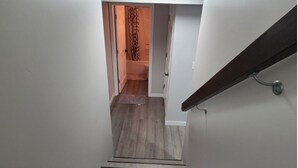 A narrow staircase with wooden steps leading to a bathroom with a shower and a towel rack. - Devonshire Cozy Haven (Winnipeg)
