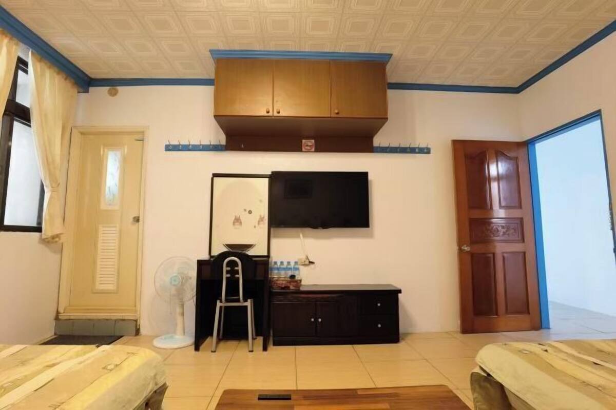 Um quarto com cama, escrivaninha com cadeira, televisão, guarda-roupa e porta.