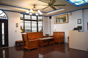 Un área de recepción con ventilador de techo, mostrador de recepción y una zona de estar con un banco y una mesa.