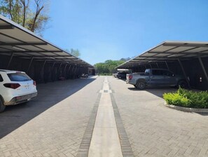 Uma área de estacionamento com toldos, um caminho pavimentado e veículos estacionados.