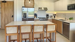 A modern kitchen with a central island, stainless steel appliances, and a hanging light fixture. - C14 - les Domus

 (Nicoya)