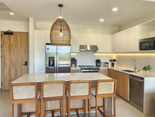 Uma cozinha moderna com uma ilha central, eletrodomésticos de aço inoxidável e uma luminária pendente.