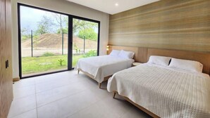 A hotel room with two beds, a large sliding glass door leading to a garden, and a ceiling fan. - C14 - les Domus

 (Nicoya)