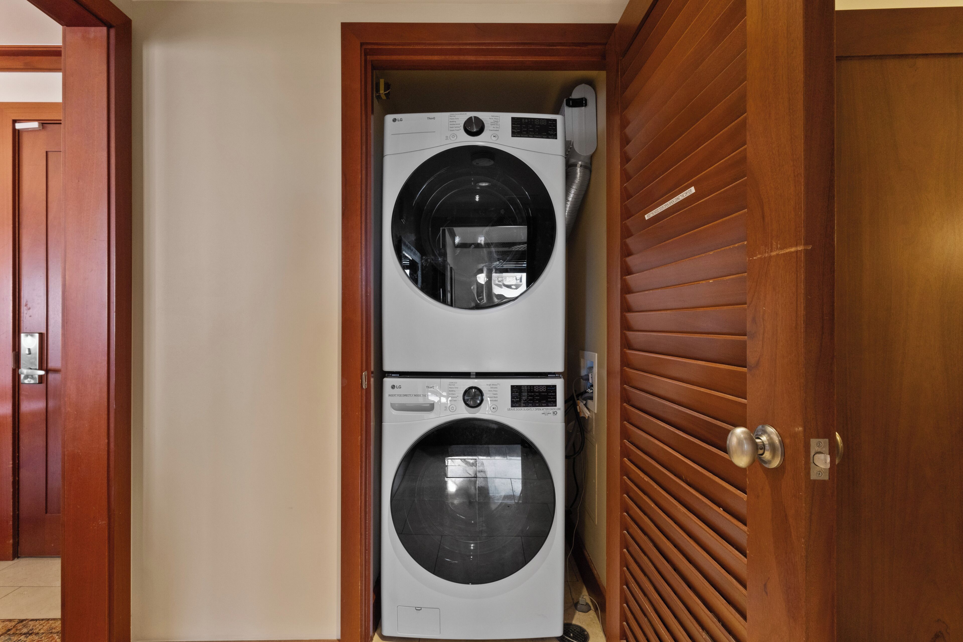 Una sala de lavandería con dos lavadoras apiladas, una puerta de madera y piso de baldosas.