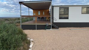 Ein modernes Haus mit überdachter Terrasse, großem Fenster und Auffahrt mit Kies.