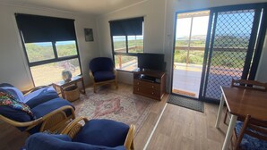 Ein Wohnzimmer mit Fernseher, Korbmöbeln und großen Fenstern mit Blick ins Freie.