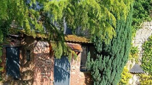 A rustic brick building with a blue door, surrounded by lush greenery and a stone pathway. - Cozy cottage in charming Les Andelys with AC, WiFi (Les Andelys)