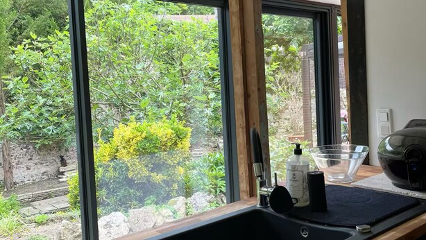 A kitchen with a wooden countertop, a black sink, and a window with a view of greenery outside. - Cozy cottage in charming Les Andelys with AC, WiFi (Les Andelys)