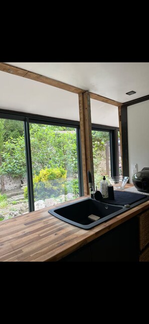 A kitchen with a wooden countertop, a black sink, and a window with a view of greenery outside. - Cozy cottage in charming Les Andelys with AC, WiFi (Les Andelys)