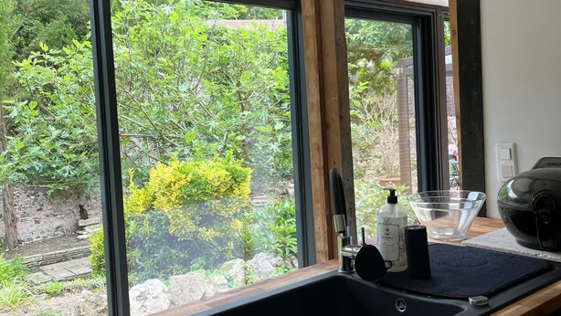 A kitchen with a wooden countertop, a black sink, and a window with a view of greenery outside. - Cozy cottage in charming Les Andelys with AC, WiFi (Les Andelys)