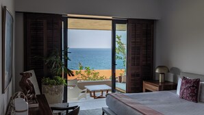 Ein Schlafzimmer mit Bett, Schreibtisch, Stuhl, Pflanze und Blick auf den Ozean.