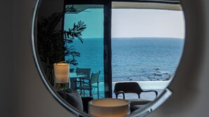 Ein runder Spiegel spiegelt ein Zimmer mit Blick auf das Meer, einen Tisch, Stühle und eine Topfpflanze wider.