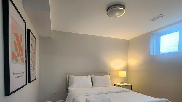 A bedroom with a bed, a nightstand, a wall-mounted lamp, and framed artwork.