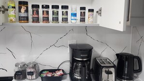 A kitchen with a marble countertop, a coffee maker, a toaster, a kettle, and a spice rack with various seasonings.