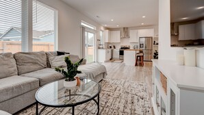 A modern living room with a sofa, a glass coffee table, and a view of a kitchen and dining area. - Brand New Family-Friendly Home for Rent in Battle Ground, WA (Battle Ground)