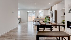 A modern kitchen with white cabinets, a stainless steel refrigerator, and a dining area with a wooden table and chairs. - Brand New Family-Friendly Home for Rent in Battle Ground, WA (Battle Ground)