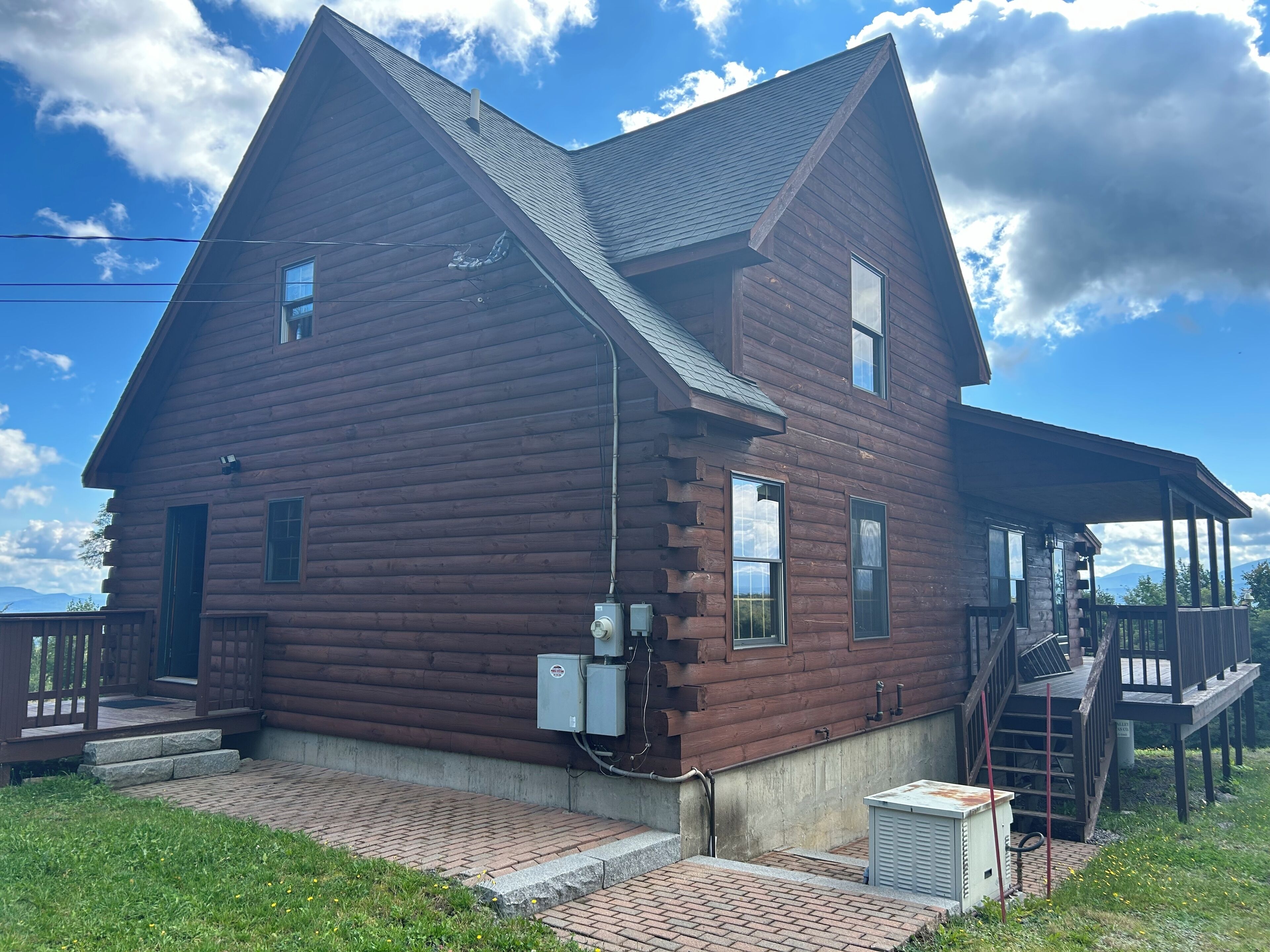 A two-story log cabin with a porch and a small deck.