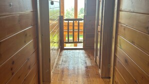 Een houten gang met een houten vloer en wanden, die uitkomt op een balkon met een balustrade.
