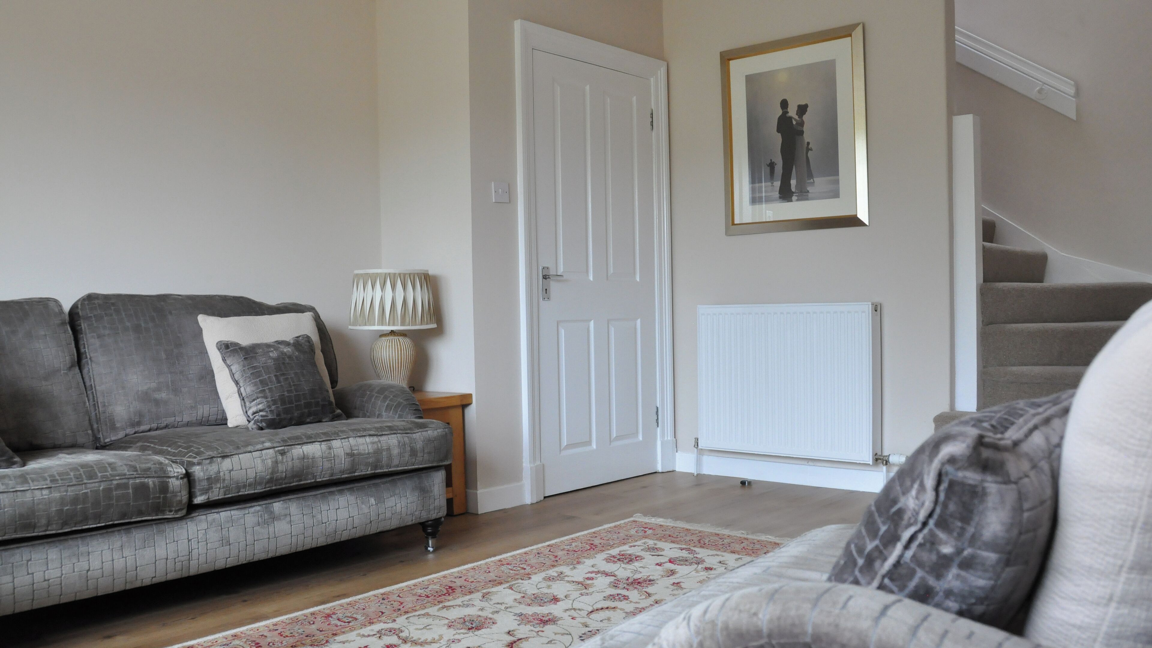 A living room with a grey sofa, a patterned rug, a lamp, and a framed picture on the wall.