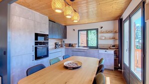 A modern kitchen with a wooden table, built-in appliances, and a large window.