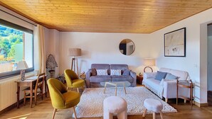 A living room with a wooden ceiling, a sofa set, a coffee table, and a small stool.