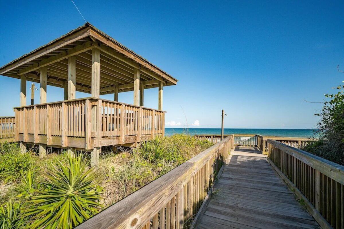 A wooden boardwalk leading to a beachside pavilion with a clear view of the ocean.