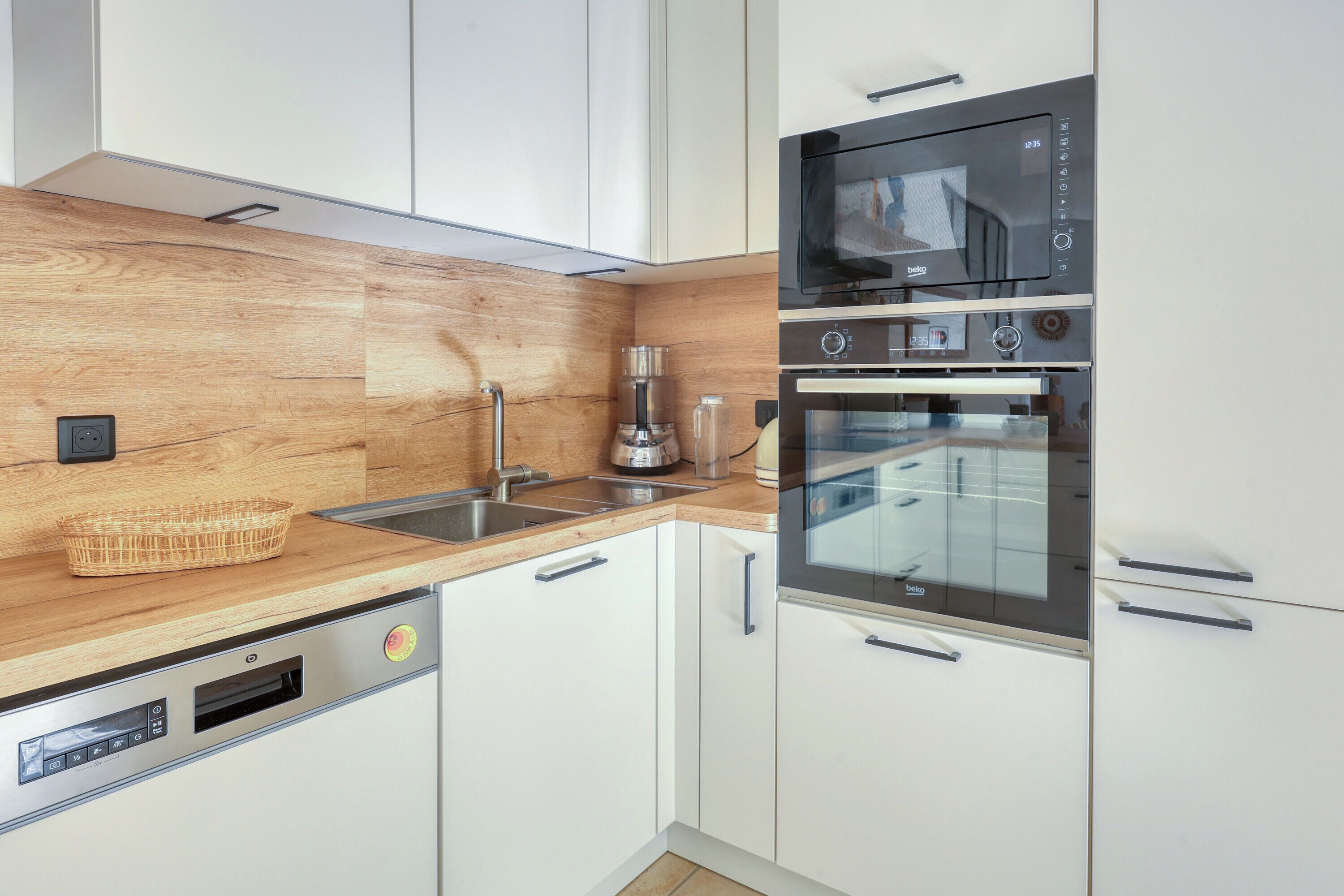 Eine moderne Küche mit weißen Schränken, einer Holz Arbeitsplatte, einem Geschirrspüler, einer Mikrowelle und einem Backofen.