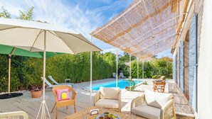 An outdoor patio with wicker furniture, a table with a plate of food, and a swimming pool in the background. - Villa Azul - Welkeys (Bandol)