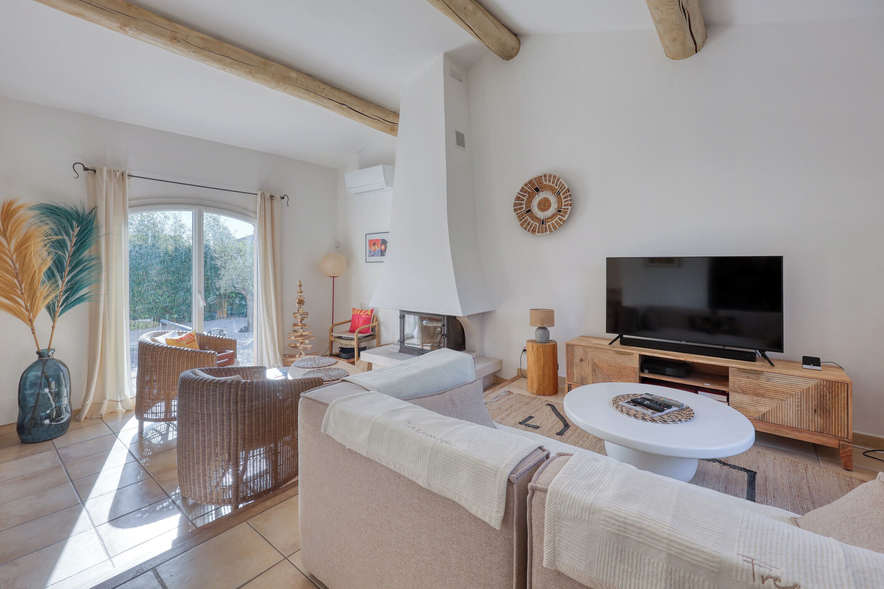 A modern living room with a large flat-screen TV, wicker furniture, and a view of the outdoors.