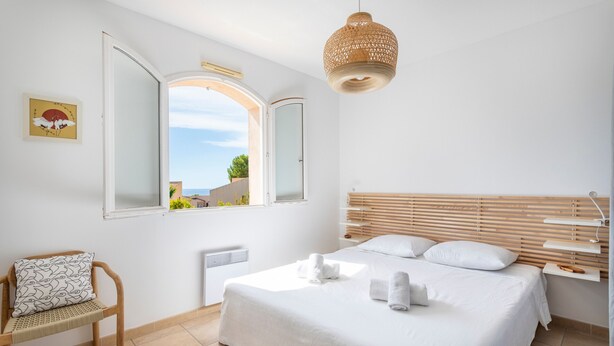 A bedroom with a bed, a chair, a window, and a hanging light fixture. - Villa Azul - Welkeys (Bandol)