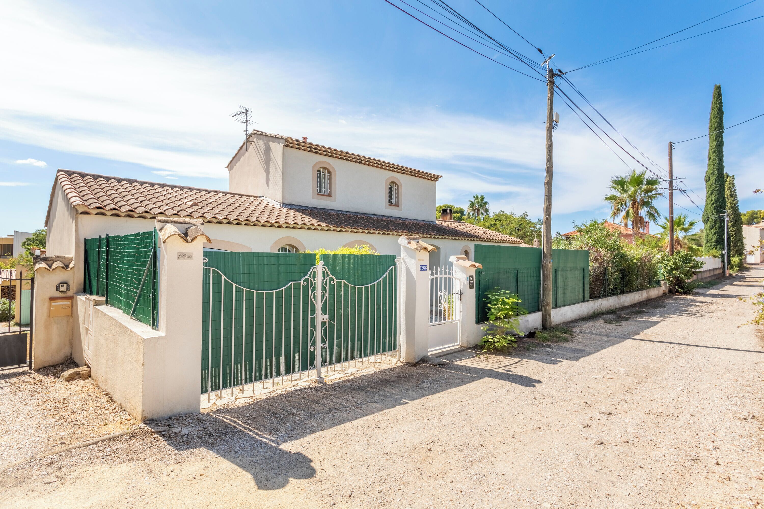 Une maison à deux étages, avec un toit en tuiles, une entrée fermée par un portail et une allée gravillonnée.