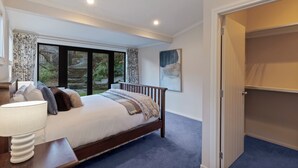 Une chambre à coucher avec un grand lit, une table de chevet avec une lampe, une fenêtre avec des rideaux et un placard.
