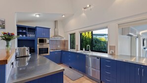 Une cuisine moderne avec des meubles bleus, des appareils en acier inoxydable et une grande fenêtre donnant sur un paysage verdoyant.