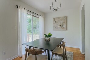 A dining area with a black table, two wooden chairs, a potted plant, a chandelier, and a large abstract painting on the wall.