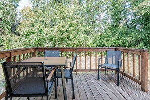 A wooden deck with a table and chairs, surrounded by dense trees.