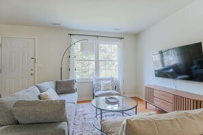 A living room with a sofa, armchair, coffee table, and a TV mounted on the wall.