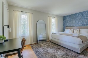 A bedroom with a bed, a desk, a chair, a mirror, and a window with curtains.