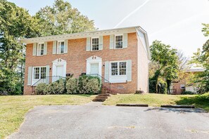 A two-story brick building with a front porch, a garage, and a well-maintained lawn.