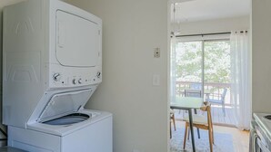 Ett tvättrum med en tvättmaskin och en torktumlare som man matar från framsidan, ett bord med stolar och utsikt över utomhusmiljön genom ett stort fönster.