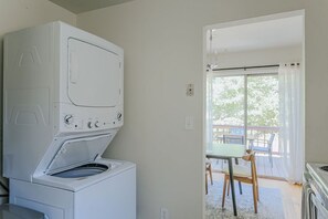 A laundry room with a front-loading washer and dryer, a table with chairs, and a view of the outdoors through a large window.