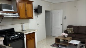 A kitchen with a stove, microwave, and wooden cabinets. There is a white door and a brown couch in the living area.