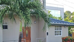 A modern house with a wooden door, a balcony, and a garden with red flowers.