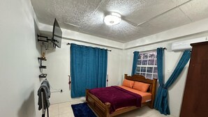 A bedroom with a bed, curtains, a ceiling fan, and an air conditioning unit.