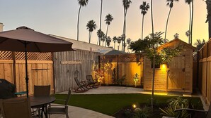 A patio area with a table and chairs, a wooden fence, and a small garden with palm trees. - 1 Block to Ocean * Brand New Remodel * Dog OK! (San Diego)
